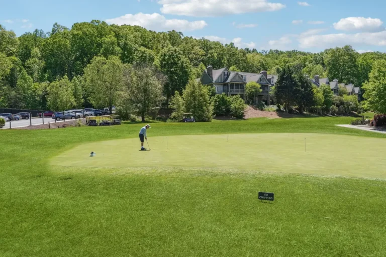 Golfer on a putting green with homes and wooded hills in the distance