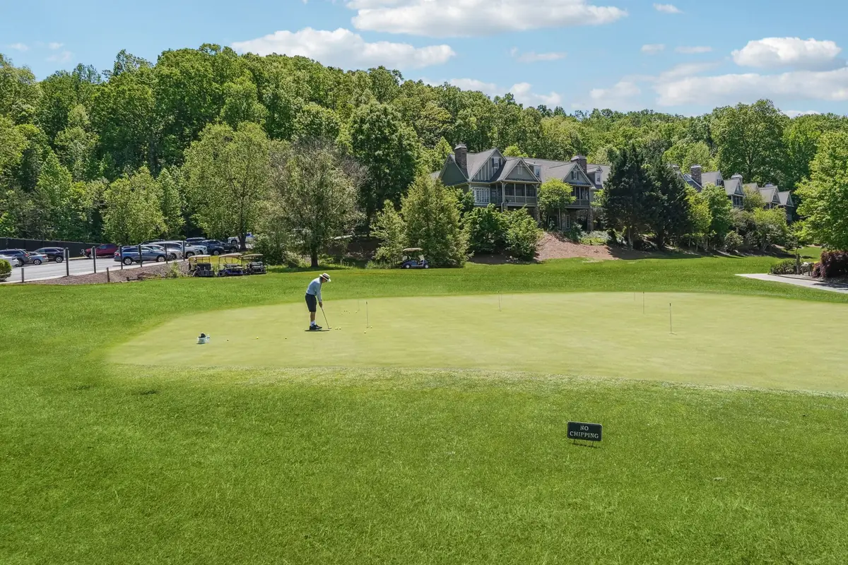 Golfer on a putting green with homes and wooded hills in the distance
